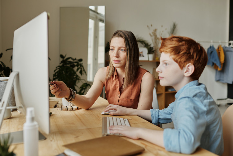 A young boy using a computer with an adult watching alongside