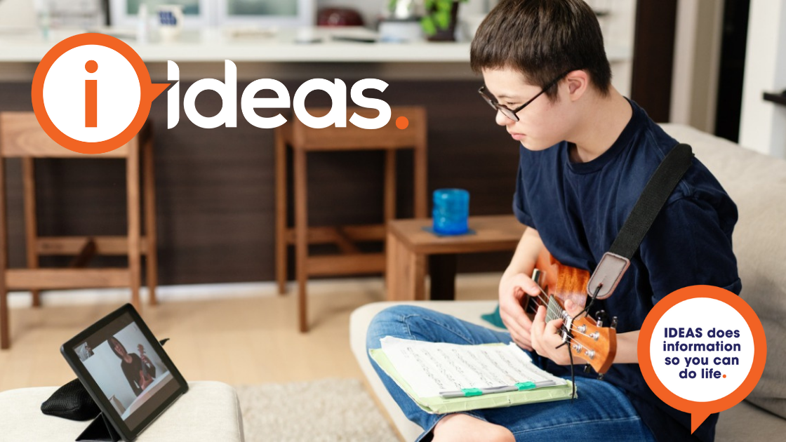 Teenage boy with down syndrome taking music lessons over the internet. He sits with music in his lap, is holding his instrument and is watching his teacher on a device