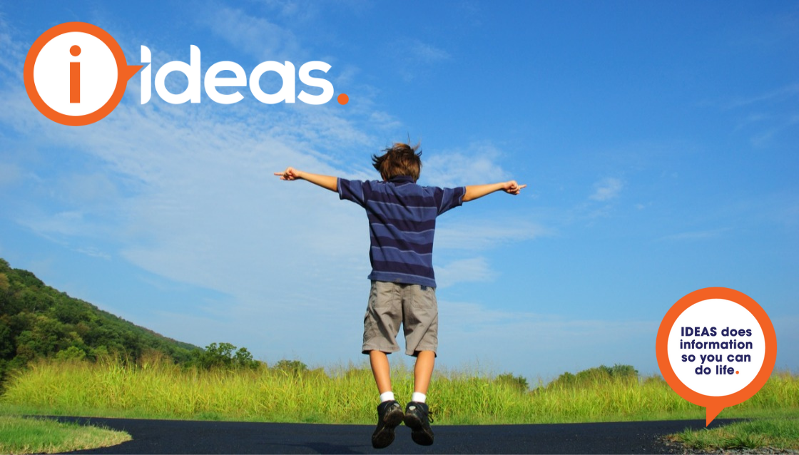 A boy standing in the middle of the path is jumping. There is green grass and blue sky with a few clouds.