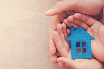 hands holding a blue house made of paper