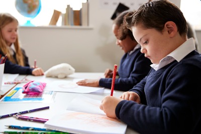 Preteen school boy with down syndrome working a desk in a classroom with a pencil in hand