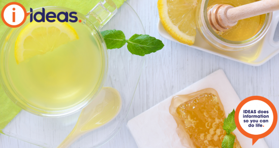 An image of a glass mug with lemon drink. Lemon, honey and comb, and a honey drizzler.