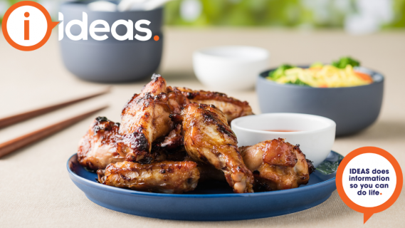 Cooked chicken wings served on a plate. To the side are chopsticks and some condiment bowls.