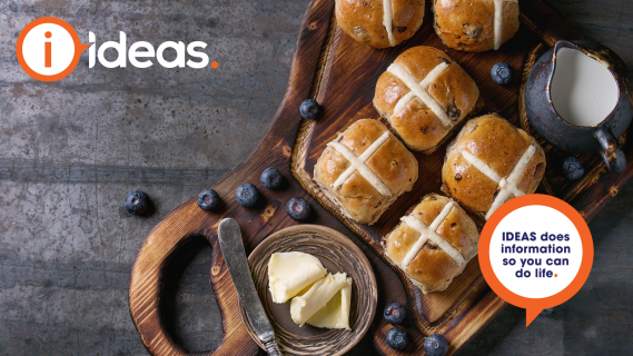 A tray of hot cross buns, milk, blueberries, and butter.